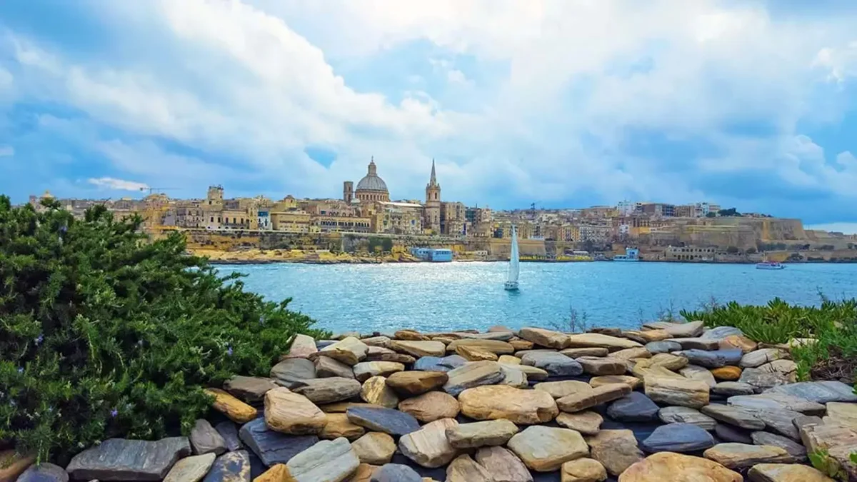 View of Valletta, Malta, from a distant rocky shore, showcasing the city’s historic buildings and harbor under a clear sky.