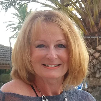 Head-and-shoulders portrait of Angela Johnson, Fellowship Support Officer for Wales for the NHS Retirement Fellowship. She is smiling in front of an outdoor background featuring palm trees.