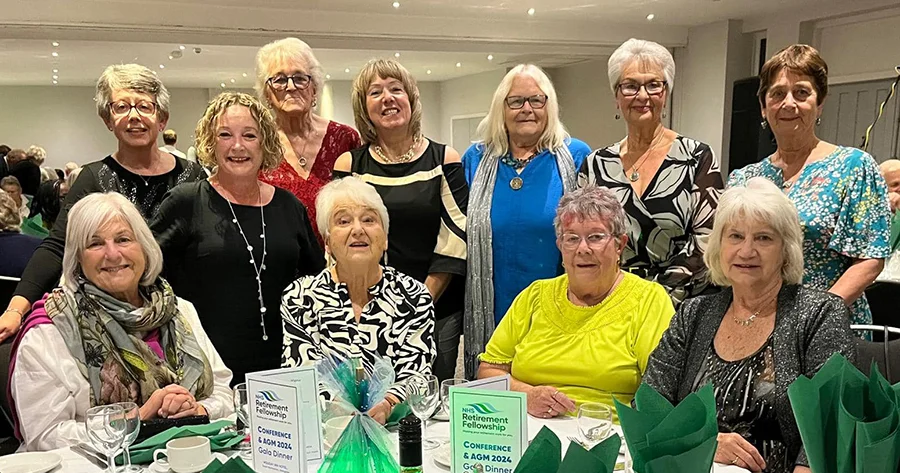 A group of NHS Retirement Fellowship members posing behind a table at the NHSRF Conference and AGM 2024, dressed in smart casual attire
